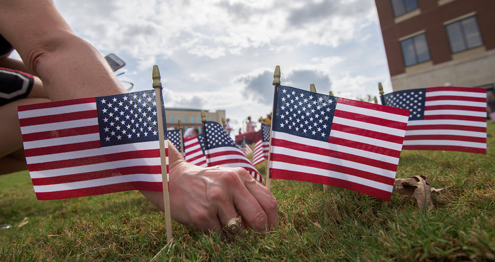 A hand placing small American flags in the ground